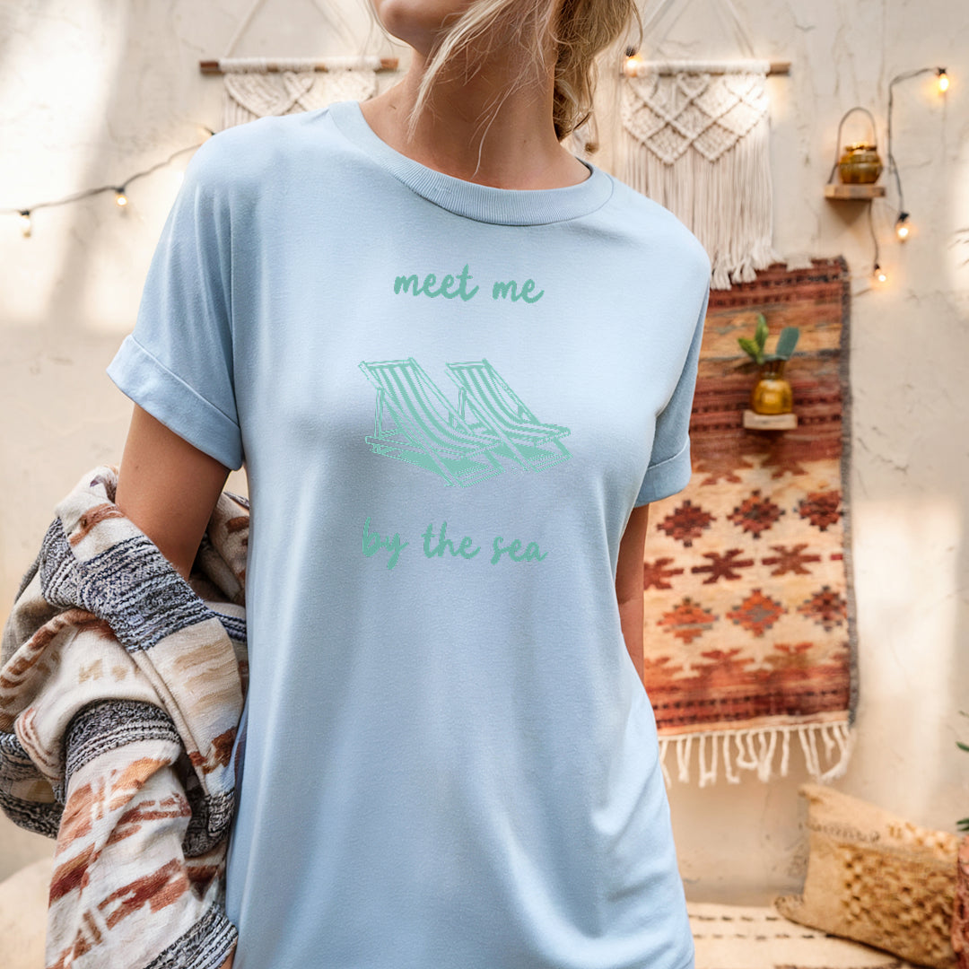 a woman wearing a t - shirt that says meet me by the sea