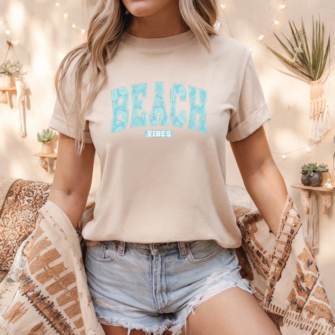 a woman sitting on a bed wearing a t - shirt that says beach