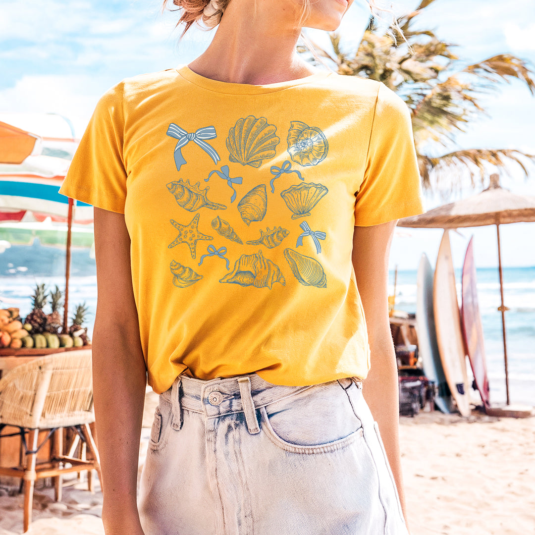 a woman standing on a beach wearing a yellow shirt