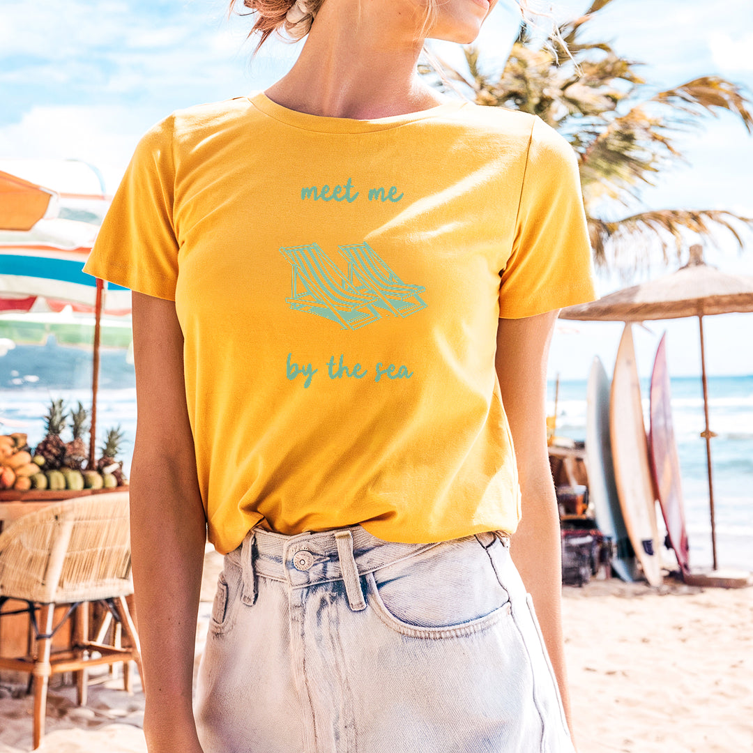 a woman standing on a beach wearing a yellow shirt