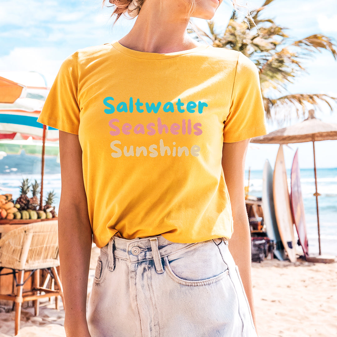 a woman standing on a beach wearing a yellow shirt
