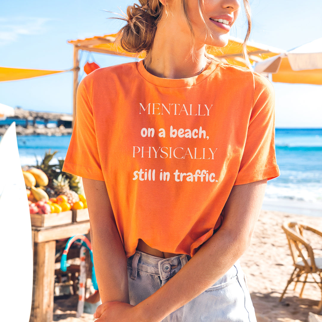 a woman standing on a beach wearing an orange shirt