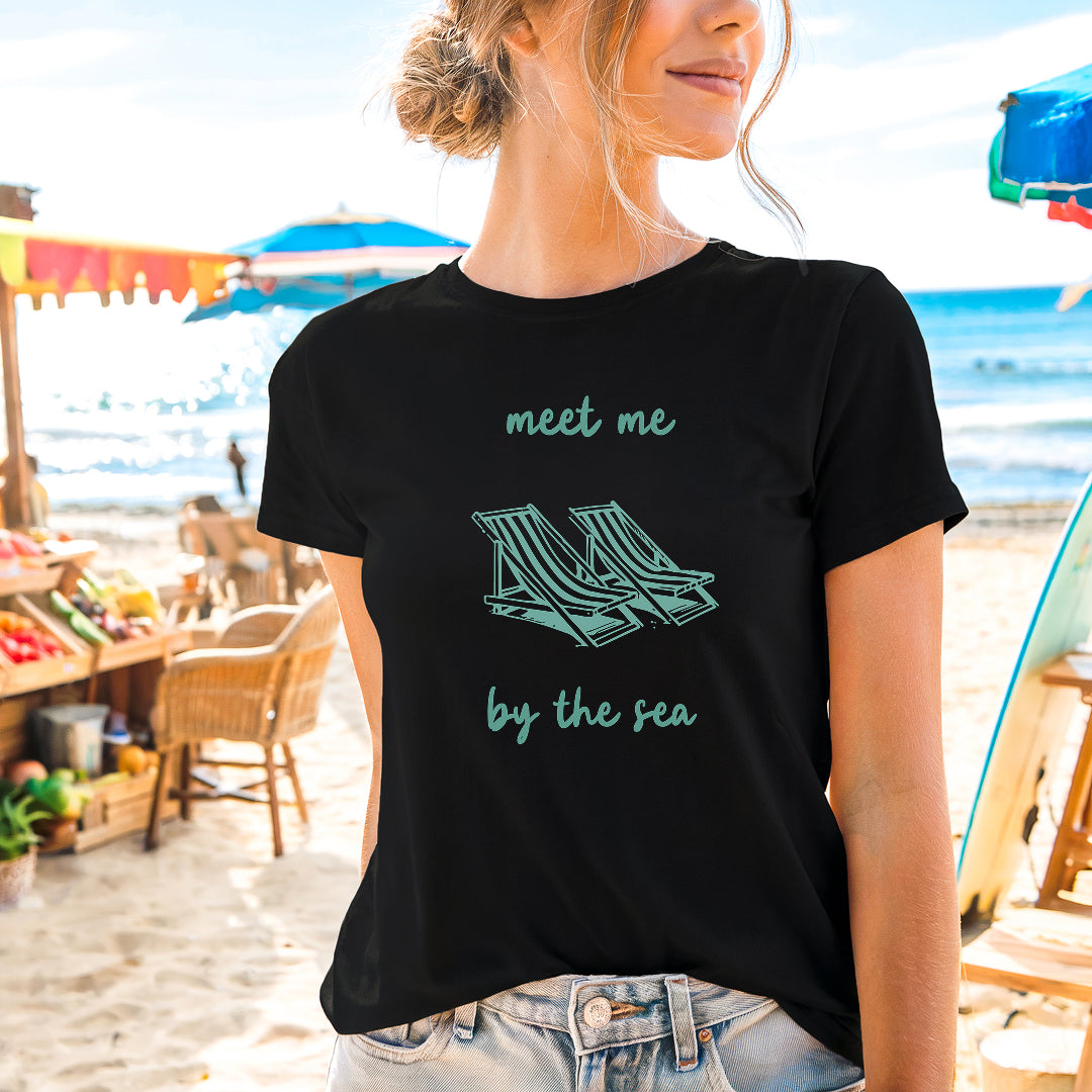 a woman standing on the beach wearing a t - shirt that says meet me by