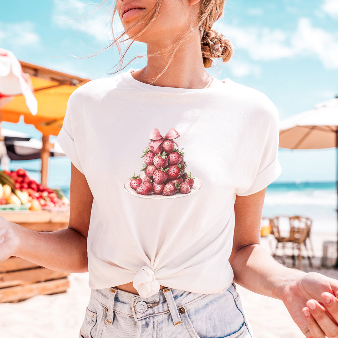 a woman standing on a beach holding a plate of strawberries