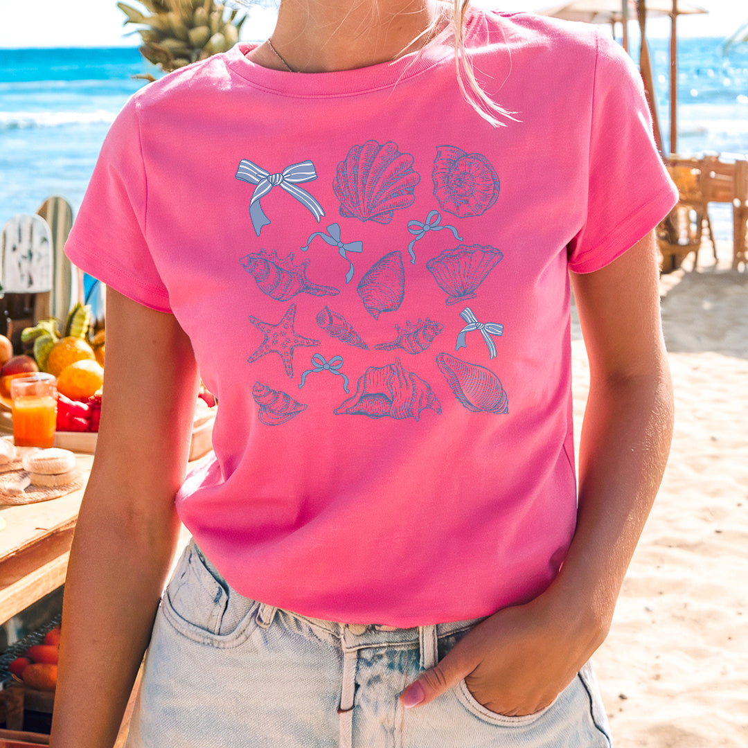 a woman standing on a beach wearing a pink shirt