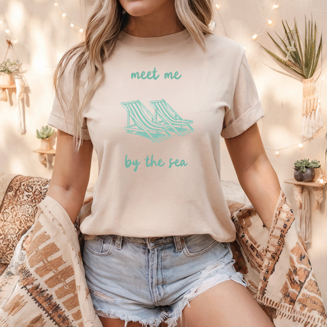 a woman wearing a t - shirt that says meet me by the sea