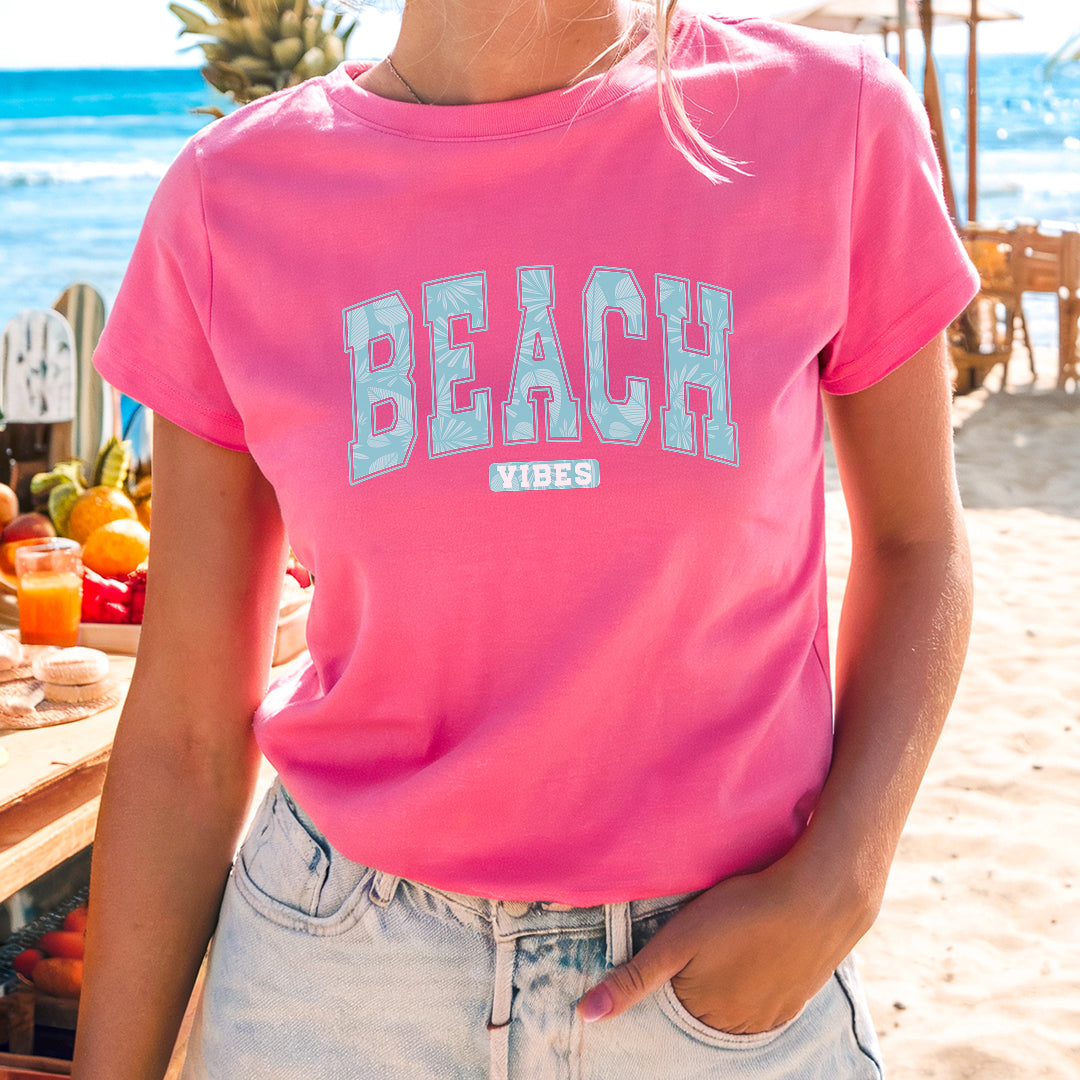 a woman standing on a beach wearing a pink shirt