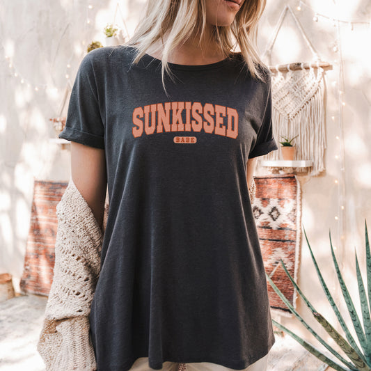 a woman standing in front of a wall wearing a sun kissed shirt