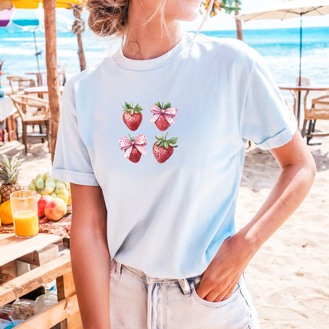 a woman standing on a beach with strawberries on her t - shirt
