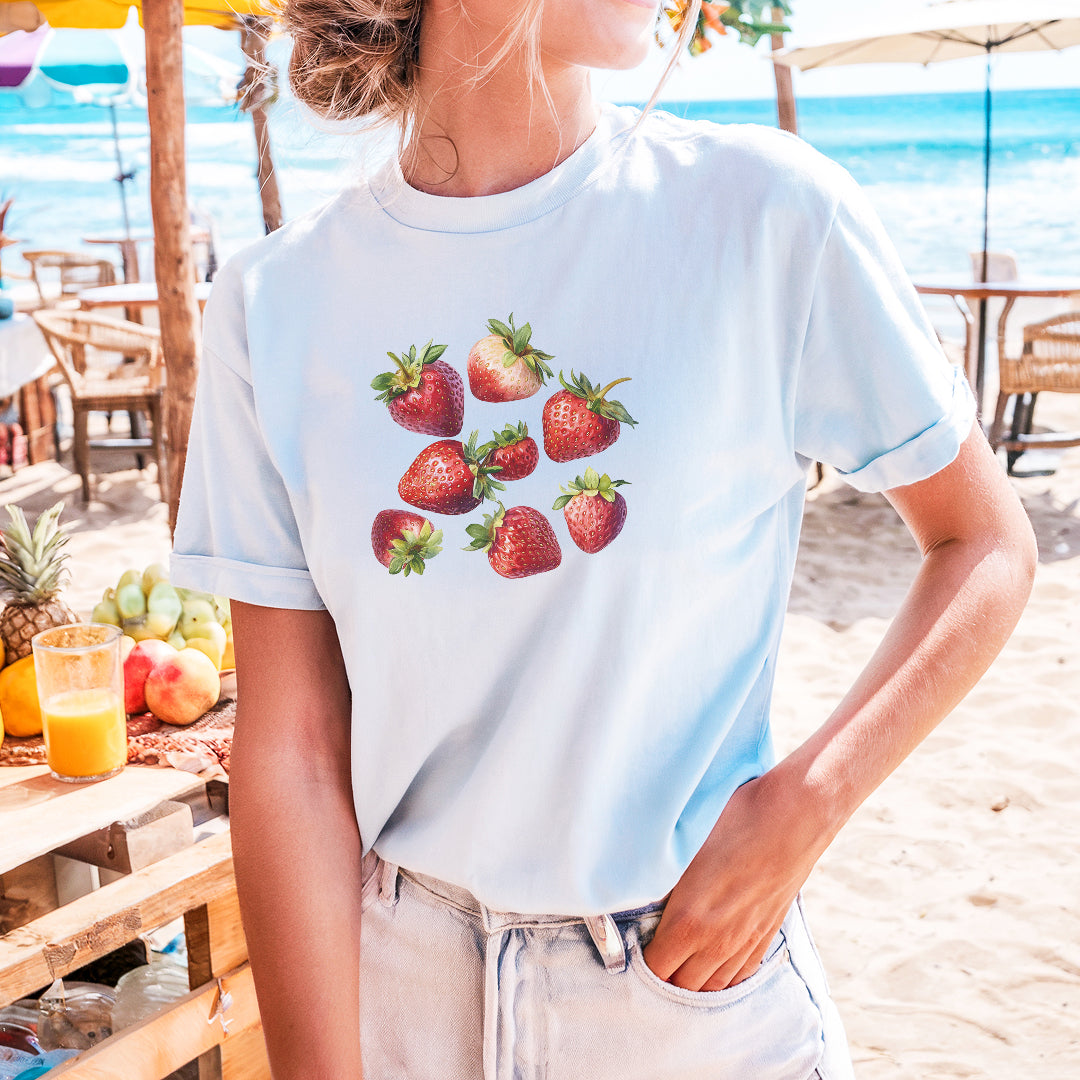 a woman standing on a beach with strawberries on her t - shirt