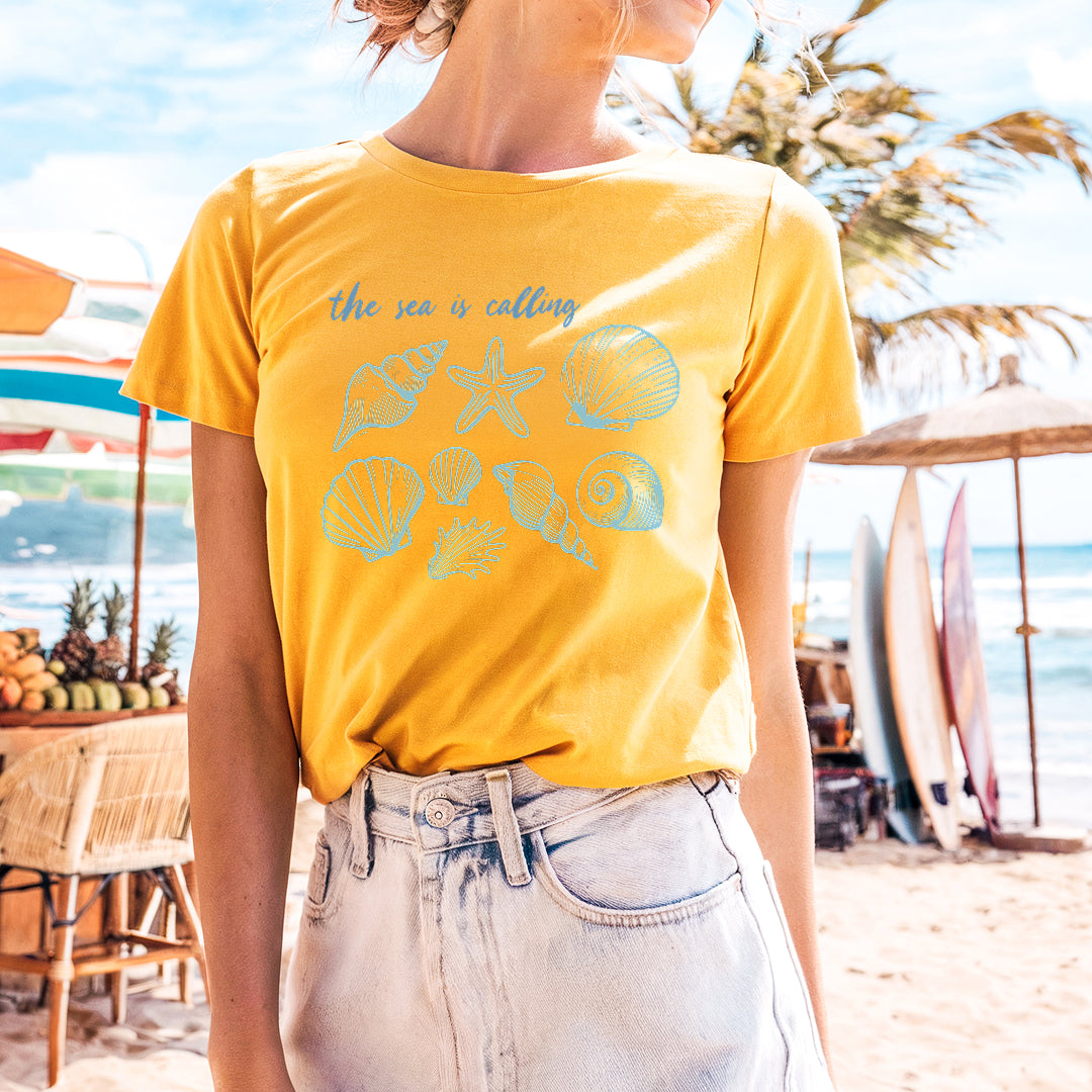 a woman standing on a beach wearing a yellow shirt